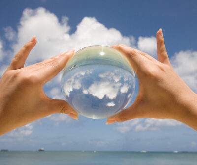 Saipan. One hands is holding a glass sphere and it projects the sky and the clouds at the beach.